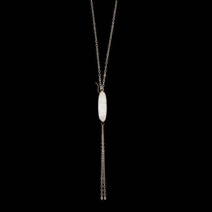 Gold lariat drop necklace with an oval white gemstone pendant against a black background.