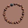 Beaded aromatherapy bracelet with brown wooden beads and a black lava rock centered on a solid brown background.