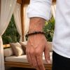Close-up of a man wearing a brown wooden and black lava stone diffuser bracelet on his wrist, dressed in a white linen shirt.