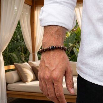 Close-up of a man wearing a brown wooden and black lava stone diffuser bracelet on his wrist, dressed in a white linen shirt.