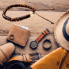 Flatlay image featuring a men's bracelet amidst travel essentials including a hat, watch, shirt, and more, depicting preparation for a stylish journey ahead.