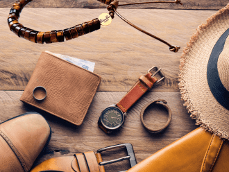 Flatlay image featuring a men's bracelet amidst travel essentials including a hat, watch, shirt, and more, depicting preparation for a stylish journey ahead.