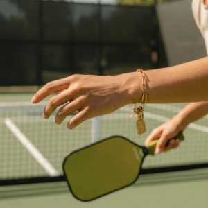 Luxury pickleball charm bracelet with link chain, paddle charm, pearl accent, and rectangular pendant in gold or silver stainless steel.