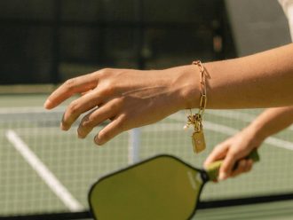 Luxury pickleball charm bracelet with link chain, paddle charm, pearl accent, and rectangular pendant in gold or silver stainless steel.