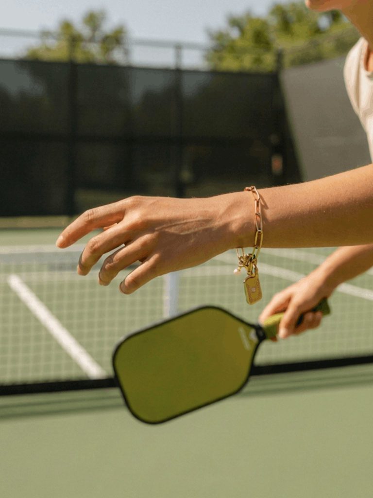 Luxury pickleball charm bracelet with link chain, paddle charm, pearl accent, and rectangular pendant in gold or silver stainless steel.