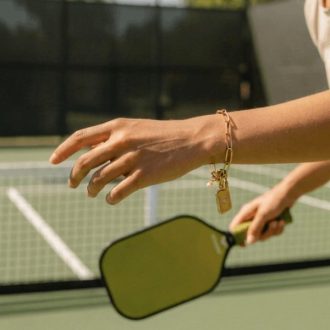 Luxury pickleball charm bracelet with link chain, paddle charm, pearl accent, and rectangular pendant in gold or silver stainless steel.