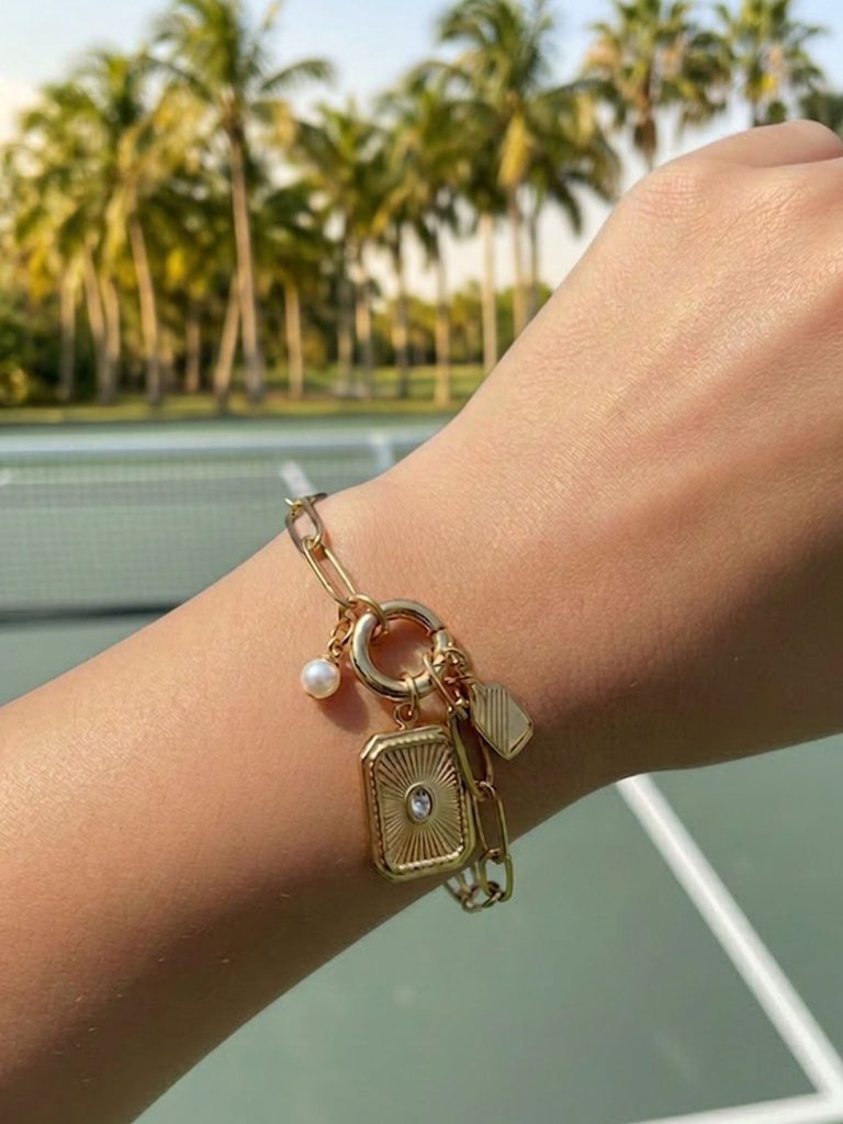 Gold pickleball charm bracelet with link chain, paddle charm, pearl accent, and rectangular pendant in gold.
