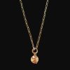 Gold paperclip link chain necklace featuring a circular spring clasp holding a round fluted sunburst disc charm, a freshwater pearl drop, and a small textured paddle tag on a black background.