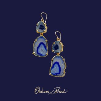A pair of handmade drop earrings by Chelsea Bond Jewelry featuring two tiers of natural royal blue agate geode slices edged in gold, hanging from 14k gold-filled earwires against a dark blue background.