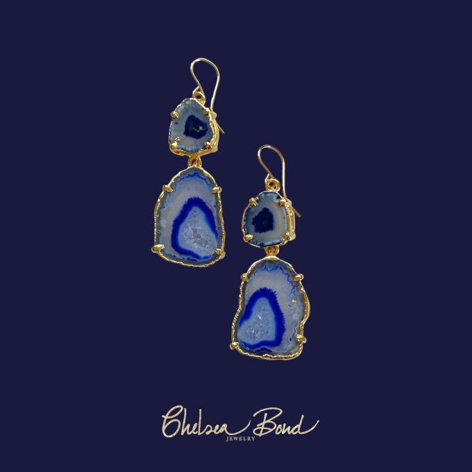 A pair of handmade drop earrings by Chelsea Bond Jewelry featuring two tiers of natural royal blue agate geode slices edged in gold, hanging from 14k gold-filled earwires against a dark blue background.