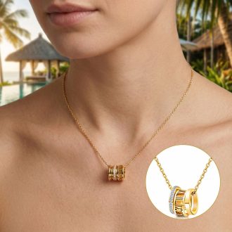 Gold waterproof necklace featuring a triple ring pendant with Roman numerals and cubic zirconia accents on woman with tropical background