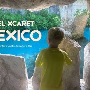 A young boy looking out at a turquoise river winding through lush jungle greenery at Hotel Xcaret in Riviera Maya, Mexico.