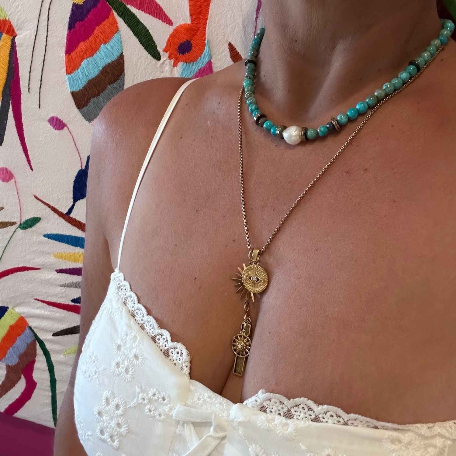 Woman wearing layered boho jewelry with a turquoise beaded baroque pearl choker and a gold celestial eye sun pendant necklace.