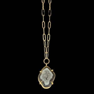 Gold druzy geode pendant necklace by Chelsea Bond Jewelry, featuring an organic-shaped gemstone set in a gold prong setting on a textured gold chain against a black background.