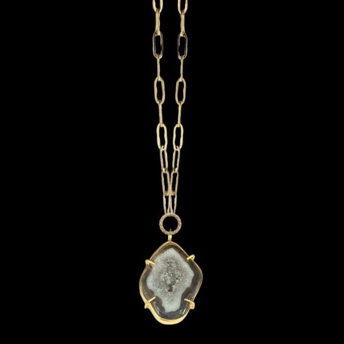 Gold druzy geode pendant necklace by Chelsea Bond Jewelry, featuring an organic-shaped gemstone set in a gold prong setting on a textured gold chain against a black background.