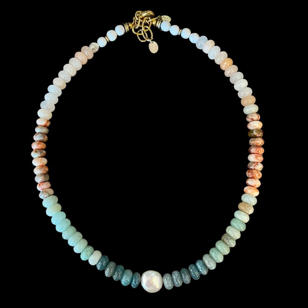 Strung natural gemstone necklace featuring smooth multi-colored rondelle beads transitioning from white to earthy orange and deep teal, centered with a large white freshwater pearl accent and an 18K gold-plated adjustable clasp on a black background.