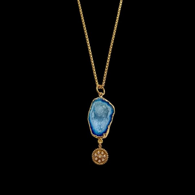 Gold box chain necklace featuring a raw gold-trimmed electric blue agate geode crystal slice dropping into a small round starburst disc charm, optimized for tropical resort jewelry displays.