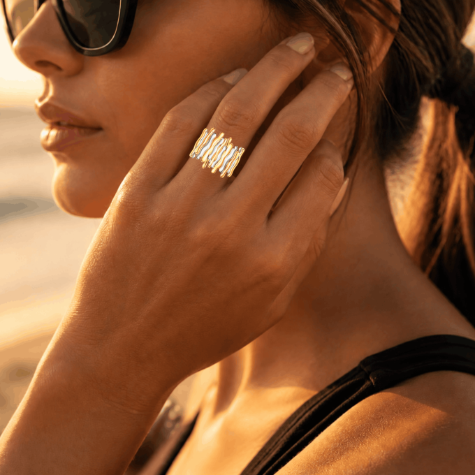 Waterproof two-tone gold and silver wavy statement ring worn on a woman's hand at the beach during sunset.