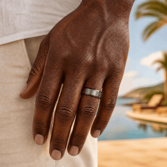 Man wearing dark silver ring on hand with beach in the background.